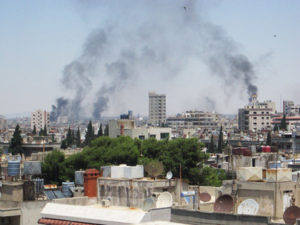 Smoke billows skyward as homes and buildings are shelled in the city of Homs, Syria. June 9, 2012. (Photo from the United Nations)