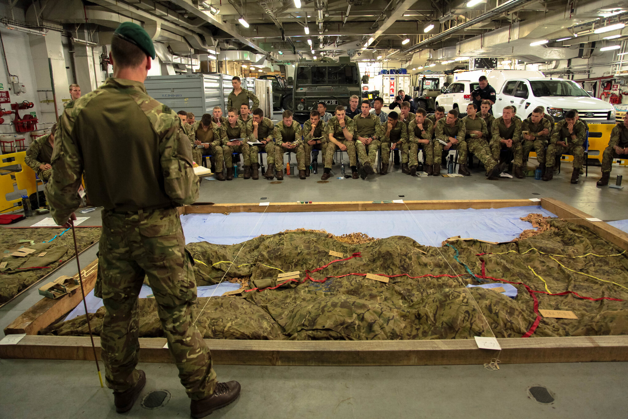 A Royal Marine commando briefs Royal Marines, U.S. Marines, Royal Navy personnel and Singaporean observers in the vehicle deck of HMS Ocean (U.K.) during BALTOPS 2016. (NATO)